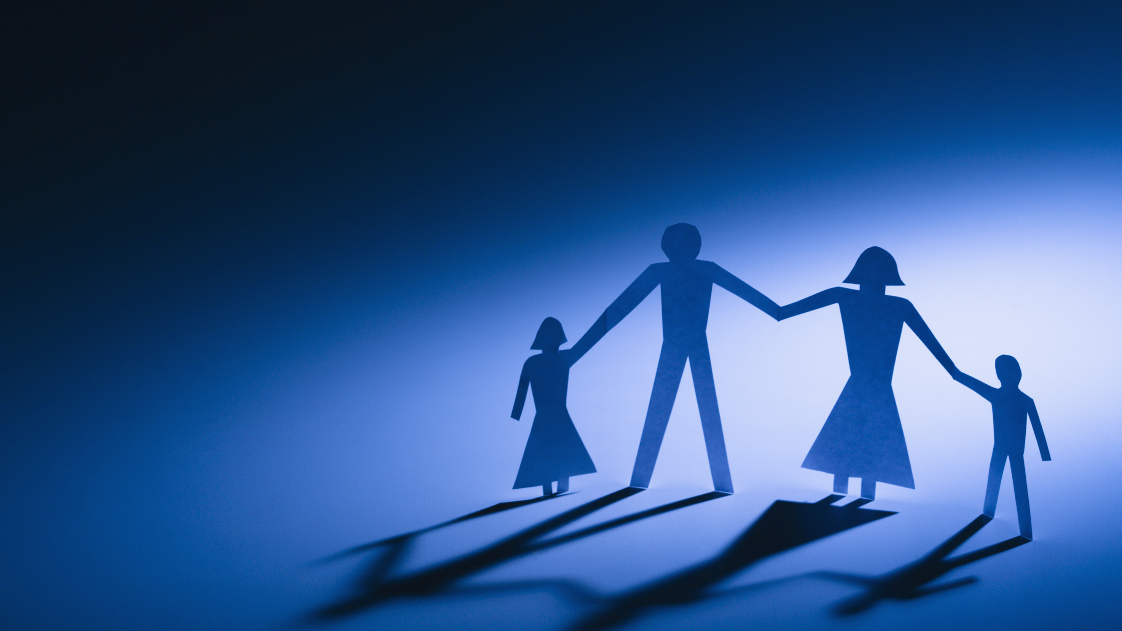 Image of a paper cutout of a family holding hands and their shadows on a paper