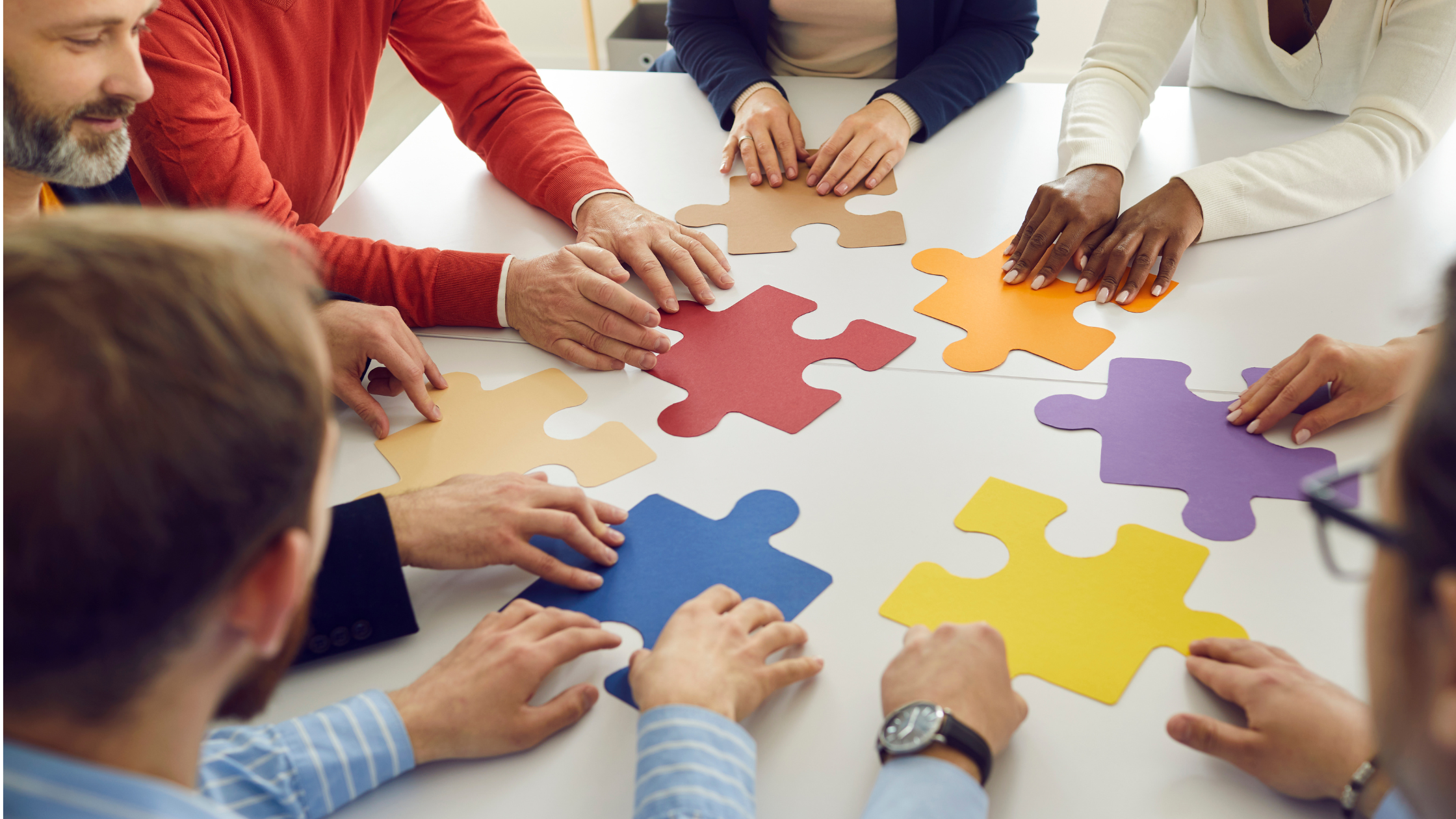 A team of people sitting around a table fitting puzzle pieces together in collaboration