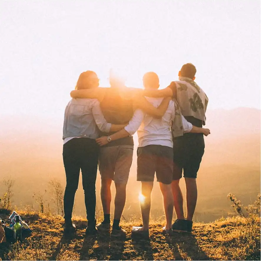 Four friends standing with arms around each other at sunset