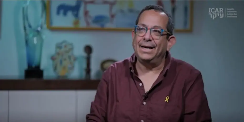 Portrait of a smiling man with glasses wearing a yellow ribbon pin